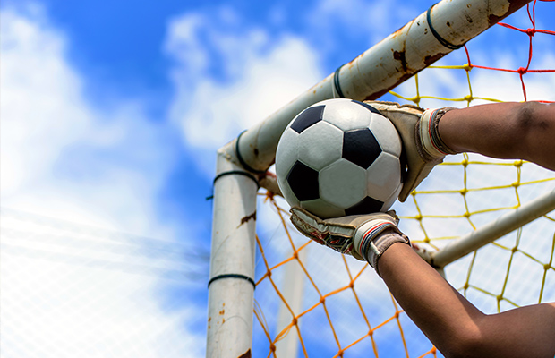 Manos de arquero de fútbol atajando pelota antes de entrar al arco